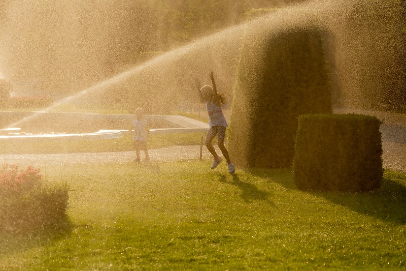 Two kids playing in a sprinkler system