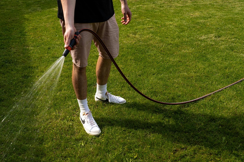 A man using a hose to water his lawn